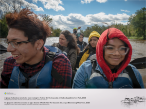 A young man and woman wearing glasses are featured in the foreground, smiling, while four of their peers are paddling the canoe in the background.