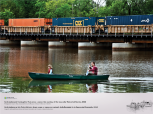 A father and his daughter enjoy canoing along the Anacostia River near Anacostia Park. A cargo train is visible in the background going over the bridge.