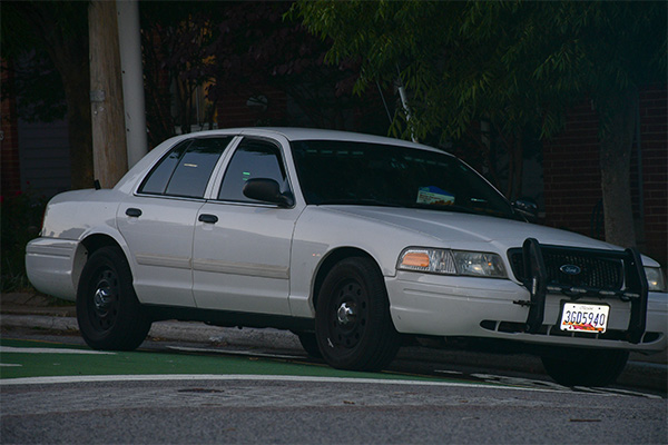 Askew’s white police cruiser is stationed on a sidestreet at dusk.