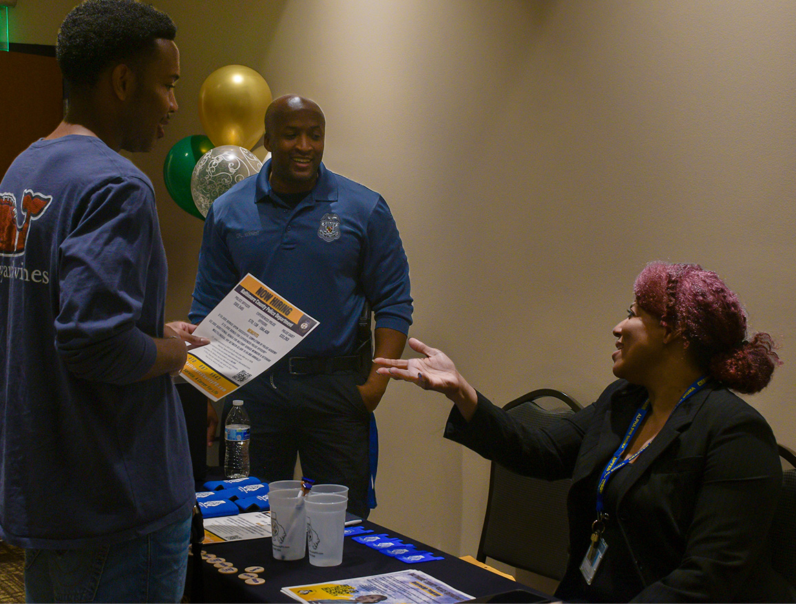 Criminal justice lecturer, Caprice Smith, engages in conversation with student Devlin Green Jr. and Cpl. Robbie Wright from a booth during Law Day at Stevenson University.