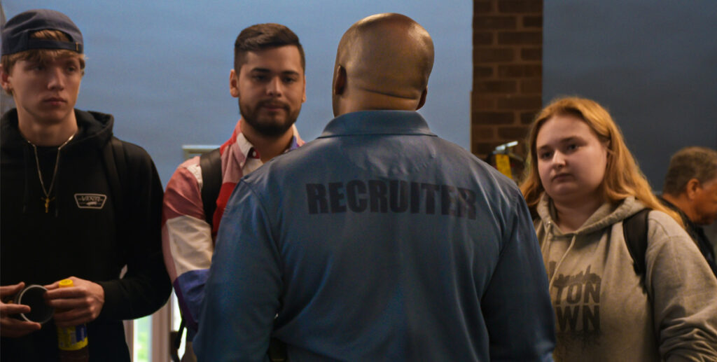 Robbie Wright speaks with three students. The back of his shirt reads, “RECRUITER.”